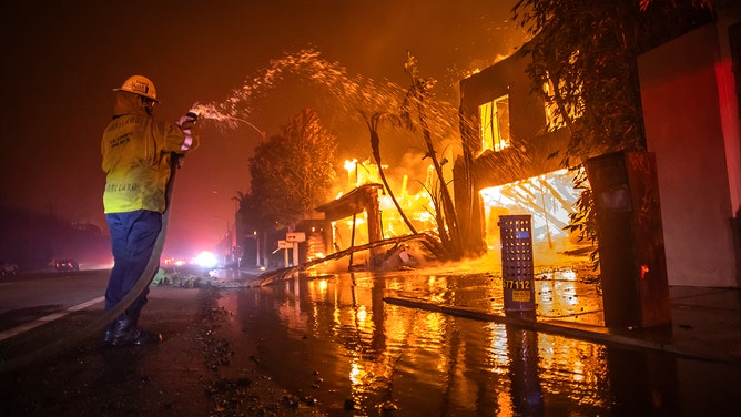 A firefighter battles the Palisades Fire while it burns homes at Pacific Coast Highway amid a powerful windstorm on January 8, 2025 in Los Angeles, California.