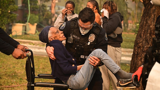 Police officers remove an elderly resident from her home during the Eaton Fire in Altadena, California, on January 8, 2025.