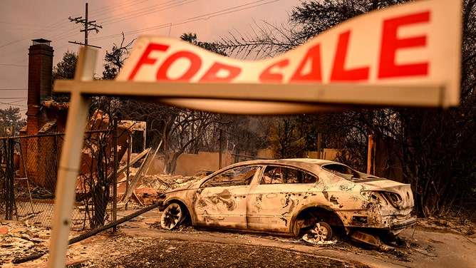 A for sale sign remains as homes and cars smolder during the Eaton fire in the Altadena area of Los Angeles County, California on January 8, 2025.