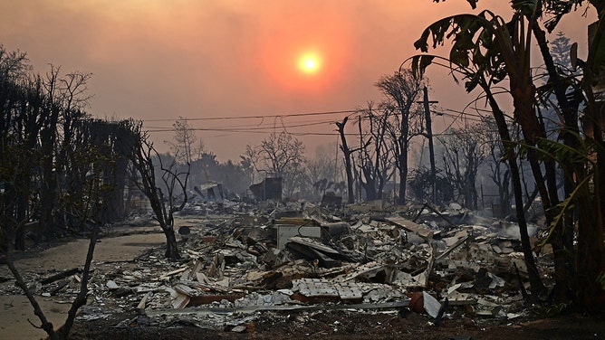 2025年1月8日、カリフォルニア州パシフィック・パリセーズで起きたパリセーズ火災の通過後、焦げた建物の上の煙の後ろに太陽が見える。