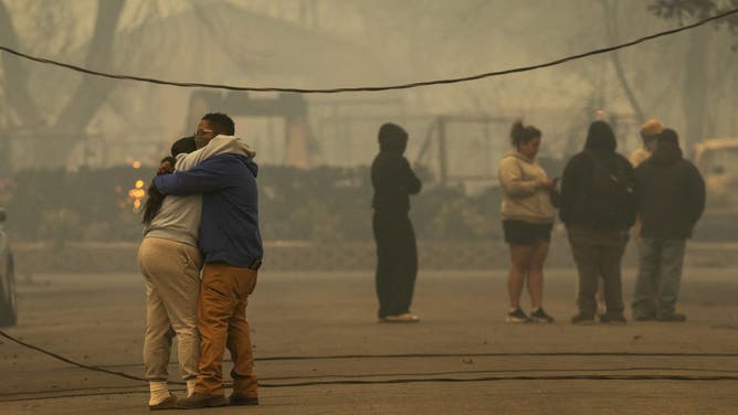 2025年1月8日、カリフォルニア州アルタデナのイートン火災でほとんどの家が焼けた地域で抱き合う人々。