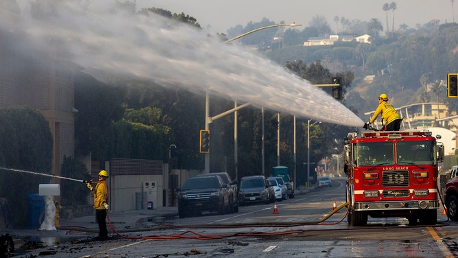 Firefighters hose down a smoldering building on the Pacific Coast Highway during the Palisades Fire in Malibu, California, US, on Thursday, Jan. 9, 2025.