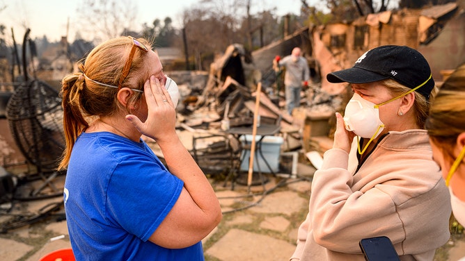 Two ladies cry while viewing their brother's burned home during the Eaton fire in the Altadena area of Los Angeles county, California on January 9, 2025.