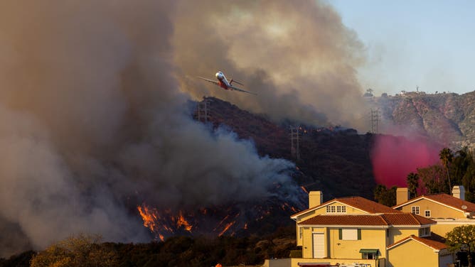 BRENTWOOD, CALIFORNIA - JANUARY 11: Fire air operations drop fire retardant, on flames from the Palisades Fire, along Mandeville Canyon, photographed from the Mountaingate development, above Mandeville, January 11, 2025, in the Brentwood community of Los Angeles, California. (Photo by Jay L. Clendenin/Getty Images)