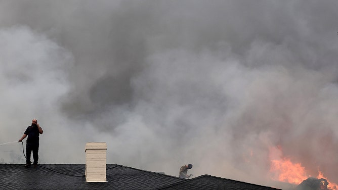 People use garden hoses in an effort to prevent a home from catching fire, as a home burns next door, during the Eaton Fire on January 8, 2025 in Altadena, California.