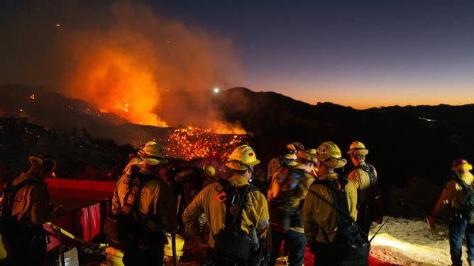 2025年1月11日、カリフォルニア州ロサンゼルスで、拡大するパリセーズ火災から煙が立ち上る中、消防士たちが活動する。