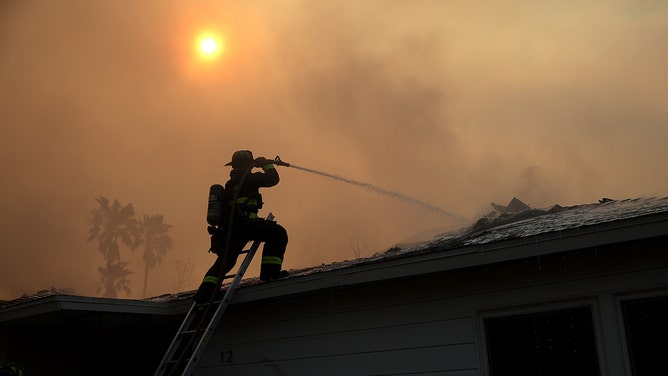 A firefighter sprays water on a burning home as Eaton Fire moves through the area on January 09, 2025 in Altadena, California.