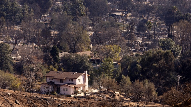 A house untouched by the Eaton Fire stands above a neighborhood destroyed by the fire in Altadena, California, on January 13, 2025.