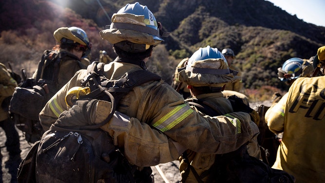 Two firefighters with the California Conservation Corps Monterey Bay Crew 1 join arms as they listen to instructions during the Palisades Fire near the Tarzana neighborhood of Los Angeles, Calif., Tuesday Jan. 14, 2025.