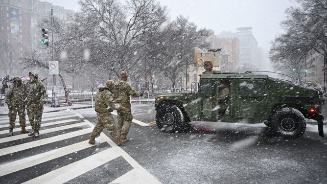 Members of the military walk towards a vehicle blocking a street as snow falls in Washington, DC, on January 19, 2025, one day before the inauguration of US President-elect Donald Trump.