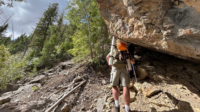 Tyson Ferriera of the Utah Field House of Natural History hiking up to the cave with tubes used to pack the bones for the trip out.