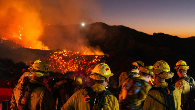 Firefighters work while smoke rises because of the growing Palisades fire in Los Angeles, California, on January 11, 2025. The Palisades Fire, the largest among the Los Angeles wildfires, pushed into new neighborhoods on January 11, prompting additional evacuations and diminishing optimism for containment. Since January 7, several fires have ravaged residential areas across the city, leaving at least 16 people dead and reducing thousands of homes to rubble. US President Joe Biden compared the destruction to a "war zone." (Photo by Ali Matin / Middle East Images / Middle East Images via AFP) (Photo by ALI MATIN/Middle East Images/AFP via Getty Images)