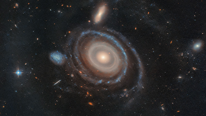 EDA 1313424, aptly nicknamed the Bullseye, is two and a half times the size of our Milky Way and has nine rings — six more than any other known galaxy. High-resolution imagery from NASA’s Hubble Space Telescope confirmed eight rings, and data from the W. M. Keck Observatory in Hawaii confirmed a ninth. Hubble and Keck also confirmed which galaxy dove through the Bullseye, creating these rings: the blue dwarf galaxy that sits to its immediate center-left.