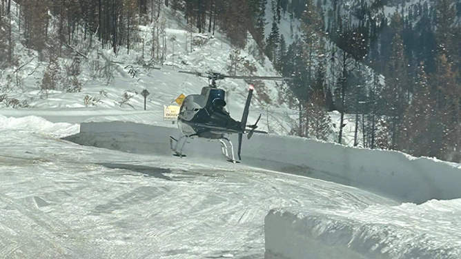 A helicopter is seen near an avalanche that closed State Highway 21 in Idaho.