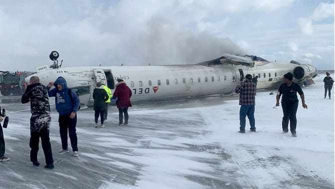 People scurry around a Delta Airlines plane that crashed upside down at the Toronto Pearson International Airport on Feb. 17, 2025, in Toronto, Canada.