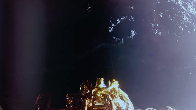 The image shows the Moon’s surface and a top-down view of the lander’s RCS thrusters (center) with a sun glare on the right side.