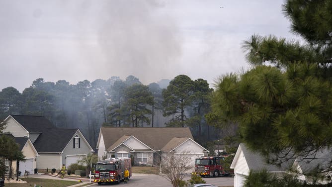 MYRTLE BEACH, SOUTH CAROLINA - MARCH 2: Smoke rises behind homes as firefighters battle a blaze in the Carolina Forest neighborhood on March 2, 2025 in Myrtle Beach, South Carolina. Multiple forest fires in the area have caused evacuations along the South Carolina coast.