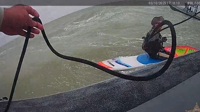 A marine officer throws a rope to the stranded windsurfer. 