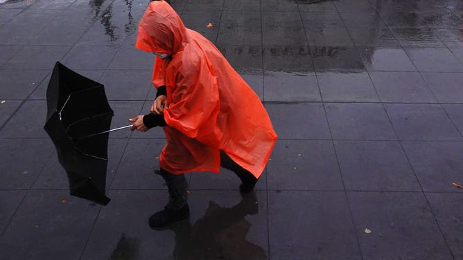 FILE: A person wearing a rain poncho struggles with their umbrella in the Brooklyn borough of New York City.