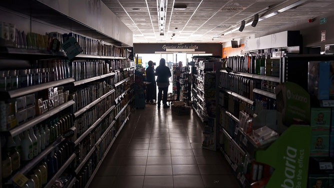 Employees stand inside a supermarket without lights in Burgos on April 28, 2025, during a massive power cut affecting the entire Iberian peninsula and the south of France.