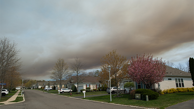 Smoke from the Jones Road Fire is seen over homes in a neighborhood in Ocean County, New Jersey, on April 23, 2025. Some 3,000 residents were evacuated in the US state of New Jersey after a wildfire exploded in size, scorching thousands of acres and threatening hundreds of structures, the state's fire service said on April 22. New Jersey had been under an official drought warning, the state's Department of Environmental Protection said in March. (Photo by Matthew Hatcher / AFP) (Photo by MATTHEW HATCHER/AFP via Getty Images)