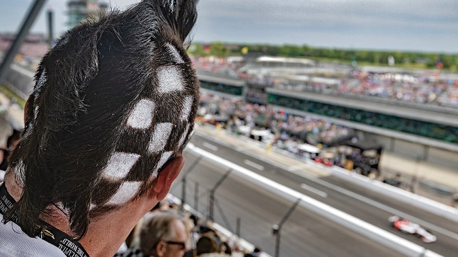 A checker headed fan awaits the checkered flag looking towards the finish line at the Indianapolis 500.