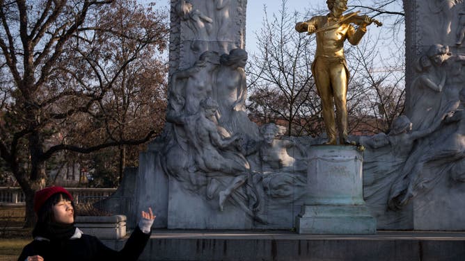 A tourist poses for a photo in front of a statue of composer Johann Strauss by sculptor Edmund Hellmer at the Stadtpark in Vienna on February 13, 2017. - The most famous waltz by Johann Strauss.