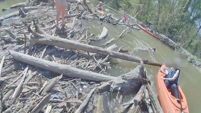 A woman clings to a log in the river as her daughter stands on a dam of logs in the river.