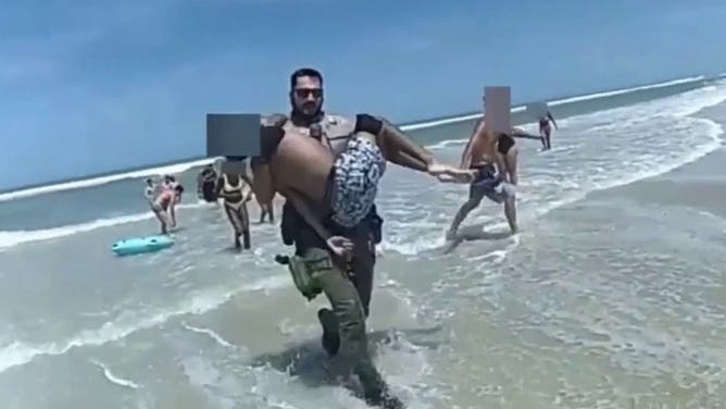 Officer carries teen from the water.
