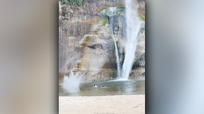 Rockfall splashes next to swimmers under Lower Calf Creek Falls.
