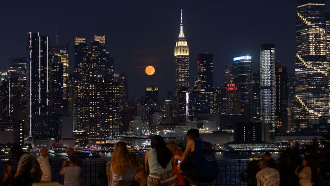 The full Strawberry Moon rises behind the Empire State Building in New York City as people watch from a park on June 21, 2024, in Weehawken, New Jersey