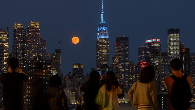 People photograph the full Strawberry Moon rise behind the skyline of midtown Manhattan and the Empire State Building in New York City on June 10, 2025, as seen from Weehawken, New Jersey.