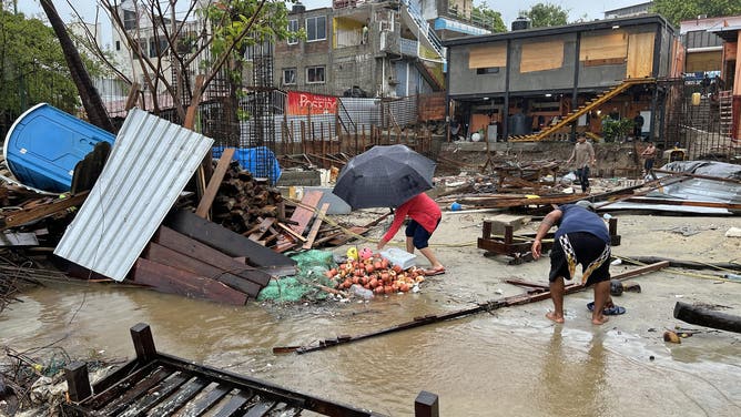 Locals walk amid debris following the passage of Hurricane Erick in Bahia Principal, Puerto Escondido, state of Oaxaca, Mexico, on June 19, 2025. Erick, a category 4 hurricane on a scale of 5, made landfall in the Mexican state of Oaxaca (west) on the Pacific coast, the United States National Hurricane Center (NHC) reported. (Photo by CARLO ECHEGOYEN / AFP) (Photo by CARLO ECHEGOYEN/AFP via Getty Images)