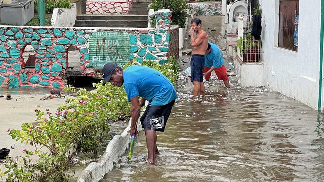 Residents try to drain water out of their houses following the passage of Hurricane Erick in Bahia Principal, Puerto Escondido, state of Oaxaca, Mexico, on June 19, 2025. Erick, a category 4 hurricane on a scale of 5, made landfall in the Mexican state of Oaxaca (west) on the Pacific coast, the United States National Hurricane Center (NHC) reported. (Photo by CARLO ECHEGOYEN / AFP) (Photo by CARLO ECHEGOYEN/AFP via Getty Images)