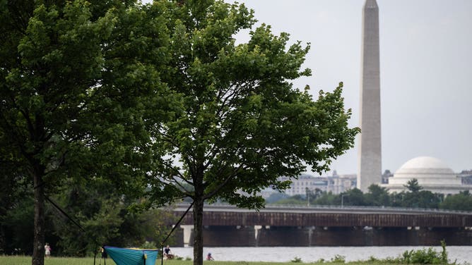 The Washington Monument is visible in the distance as a man sleeps in a hammock at Gravely Point during a severe heat wave in Arlington, Virginia on June 22, 2025. The United States is experiencing its first significant heat wave of the year, which began on June 20 across the Great Plains and expanding into parts of the Midwest and Great Lakes over the weekend, according to the National Weather Service (NWS). (Photo by ANDREW CABALLERO-REYNOLDS / AFP) (Photo by ANDREW CABALLERO-REYNOLDS/AFP via Getty Images)