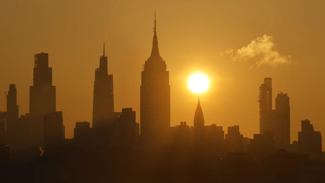 JERSEY CITY, NJ - JUNE 19: The sun rises behind the skyline of midtown Manhattan and the Empire State Building in New York City, a day ahead of the summer solstice and an expected heatwave on June 19, 2025, as seen from Jersey City, New Jersey.