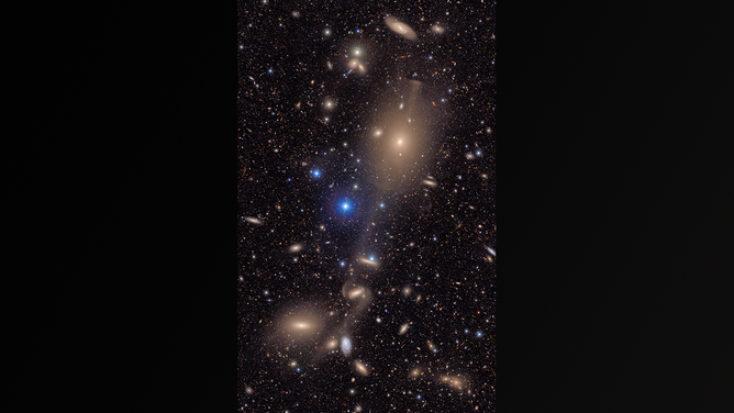 Bright stars in the Milky Way galaxy shine in the foreground and many distant galaxies are in the background.