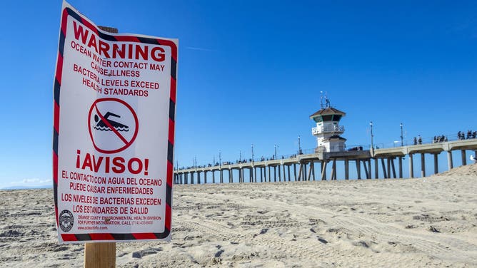 Huntington Beach, CA - January 01: A sign in the sand near the Huntington Beach Pier warns beach goers of high bacteria levels in the water due to a sewage spill on Saturday, January 1, 2022, in Huntington Beach.