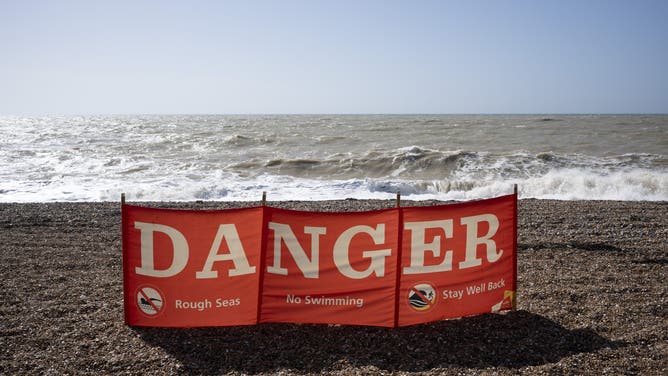 A seascape of a danger banner telling swimmers not to enter the water due to rough seas.