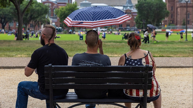 People sit as it rains National Mall ahead of the annual fireworks display on July 4, 2024 in Washington, DC.