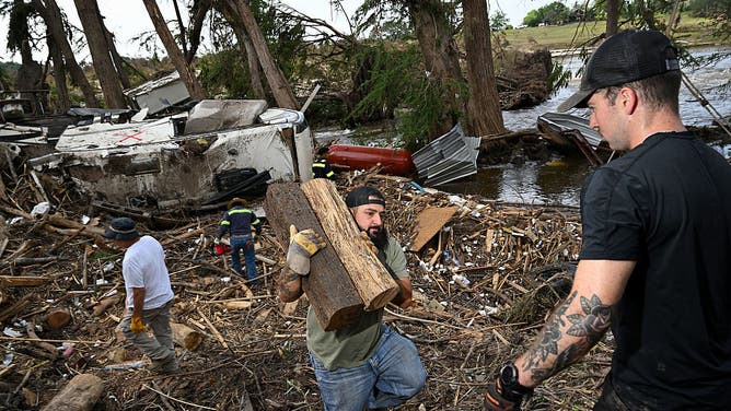 Volunteers remove trees damaged in the Central Texas floods along the Guadalupe River as they search for victims on July 9, 2025 in Center point, Texas