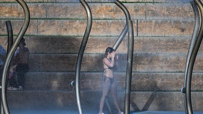 A woman washes her face on the splash pad as the region is under an extreme heat warning in Miami Beach, Florida, on July 25, 2025.