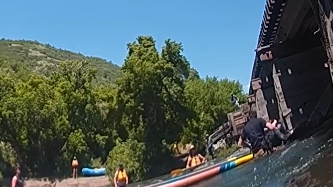 The ranger cuts the leash to the paddleboard off the woman's leg while they work to hold her up.