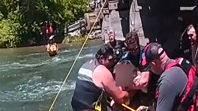 Multiple people help carry the woman back to shore after she is freed from the bridge and the rushing water.