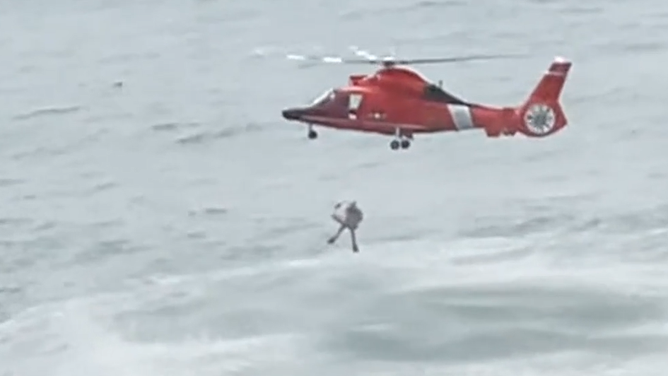The rescue swimmer and girl are carried back up into the helicopter.