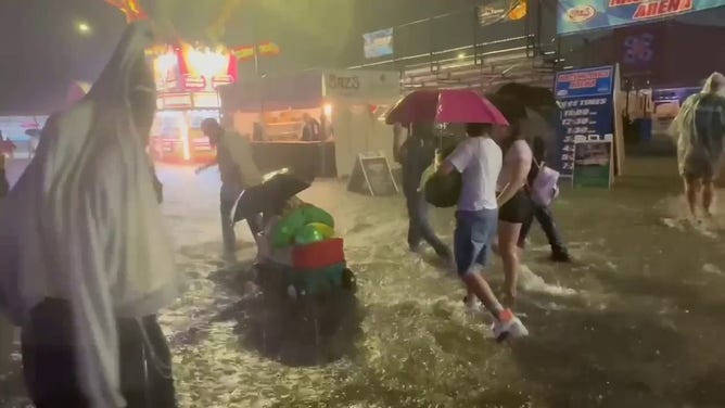 This image shows people wading through floodwaters at the Wisconsin State Fair in West Allis on Saturday, Aug. 9, 2025.