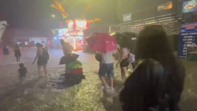 This image shows people wading through floodwaters at the Wisconsin State Fair in West Allis on Saturday, Aug. 9, 2025.