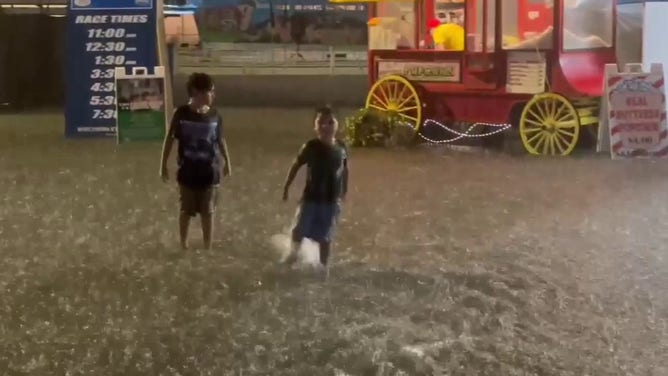 This image shows people wading through floodwaters at the Wisconsin State Fair in West Allis on Saturday, Aug. 9, 2025.