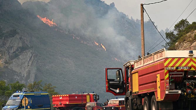 This photograph shows French firefighters engines parked on front of a wildfire near Fraissé-des-Corbières, southwestern France, on August 6, 2025. A wildfire has killed one person and injured nine others, scorching 11,000 hectares as firefighters work to contain the blaze, local officials said. The fire, which started the day before, has destroyed or damaged 25 homes in the southern Aude department, where more than 1,800 firefighters have been battling to control what is now the largest wildfire in France this summer.