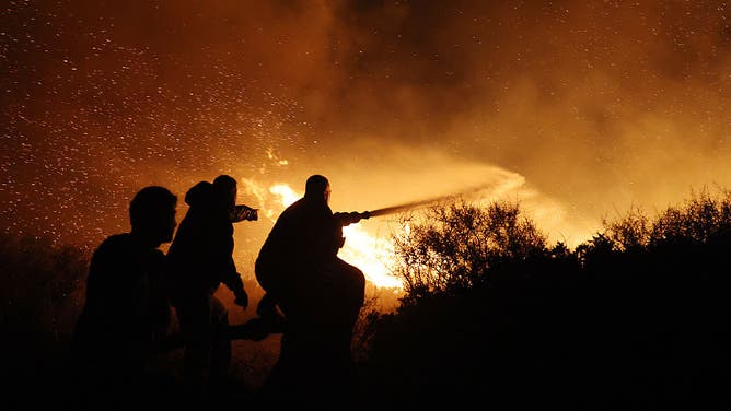 People attempt to battle a raging wildfire as flames and embers light up the night sky near the town of Keratea, southeast of Athens, Greece on August 08, 2025.
